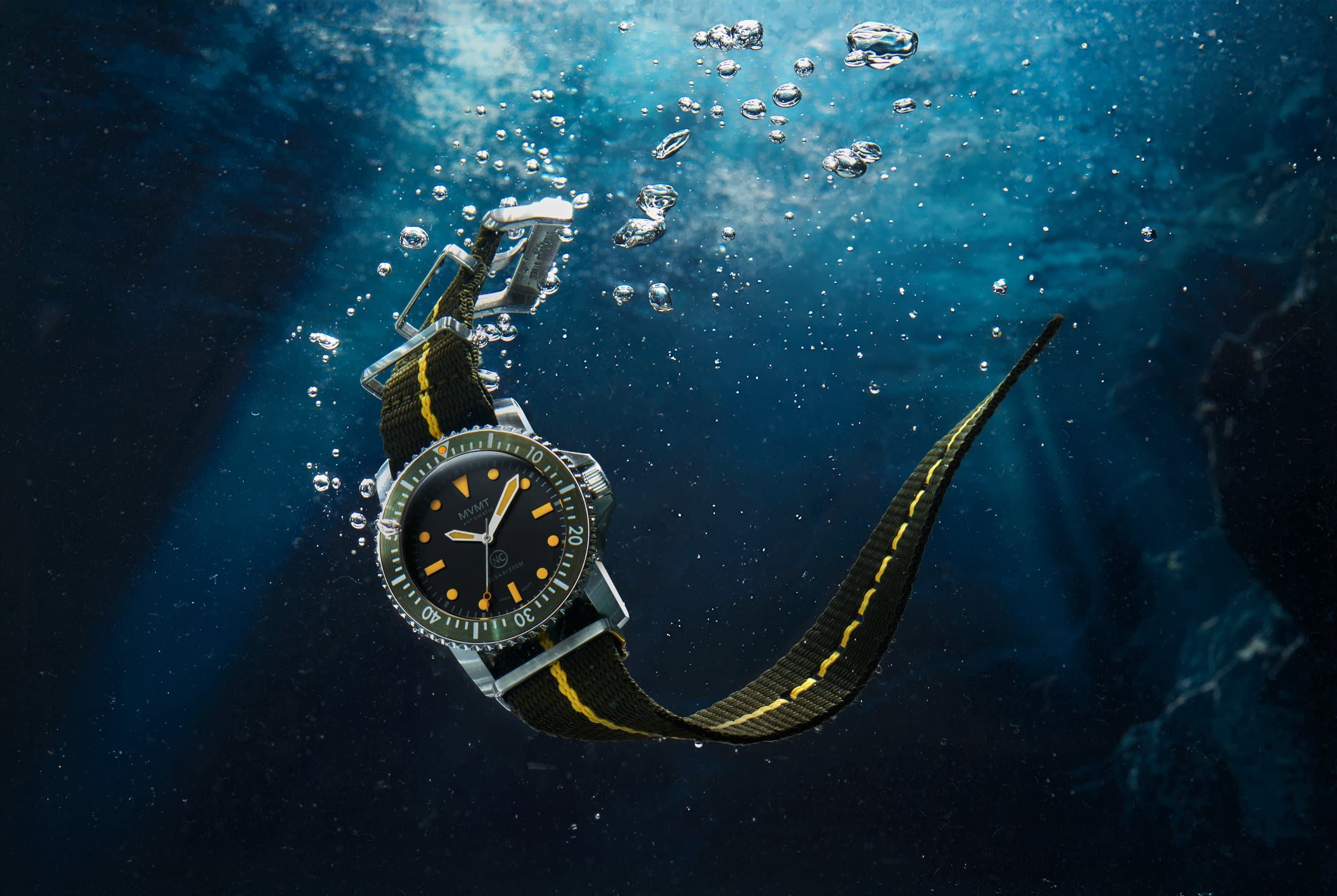 A dive watch on a striped NATO strap suspended underwater among rising bubbles