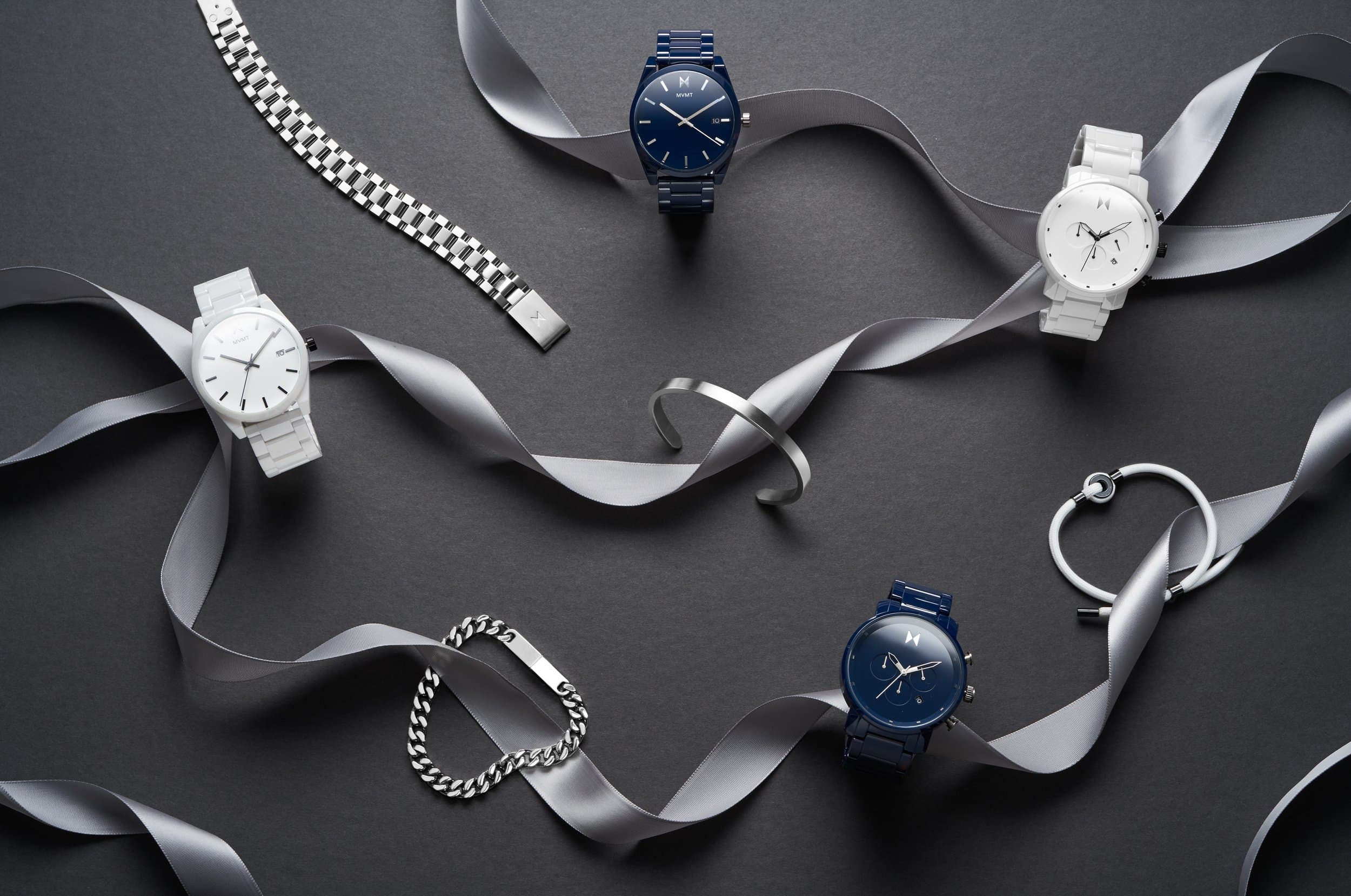 White and navy watches and silver jewelry arranged with a gray silk ribbon on a dark surface