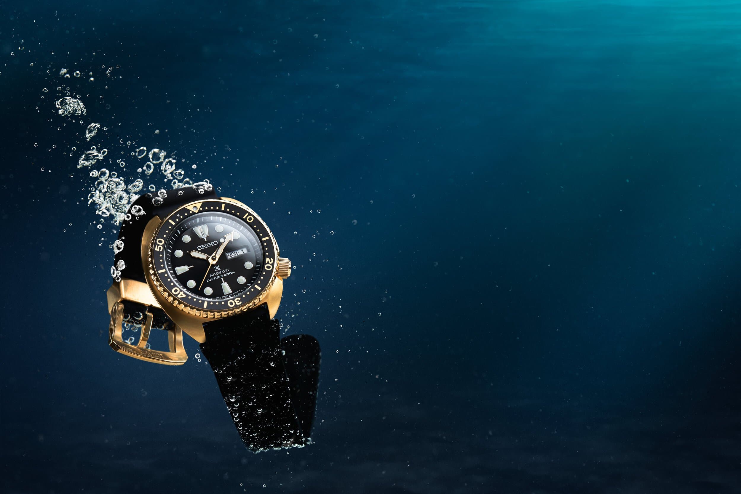 A gold-cased Seiko dive watch underwater with a trail of bubbles