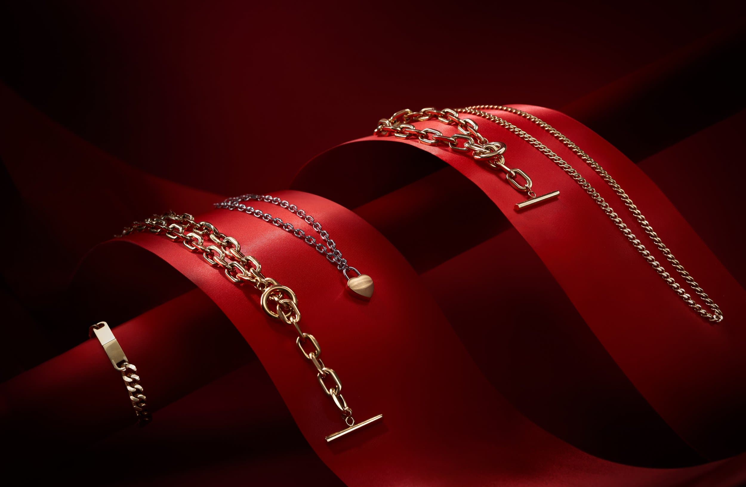 Gold and silver chains draped across a curling red silk ribbon