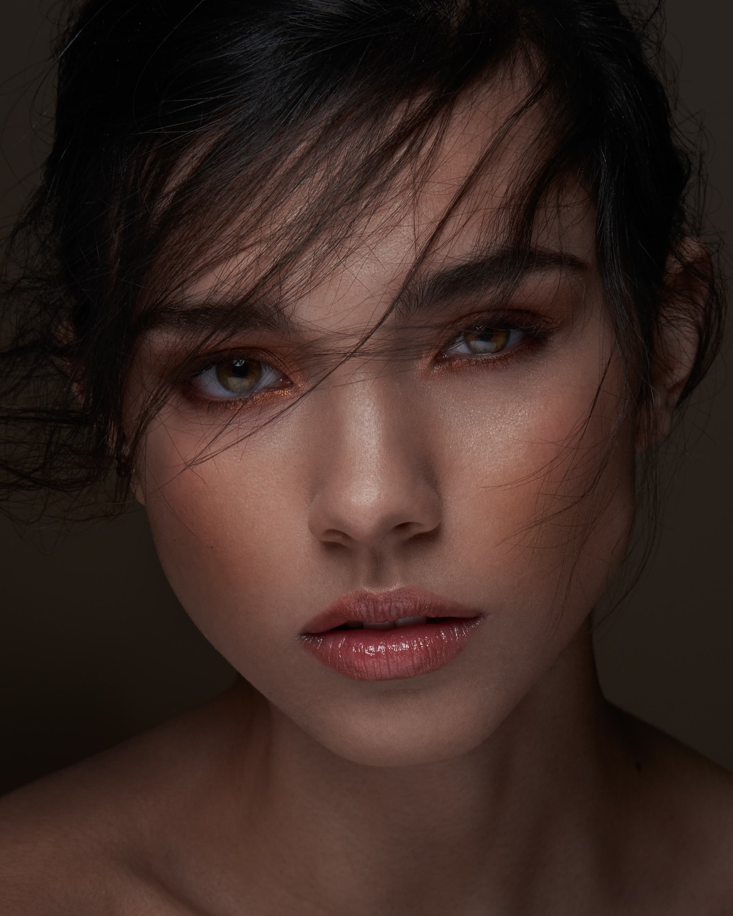 A low-key beauty portrait of a woman with dark hair and copper eyeshadow against black
